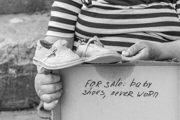 Black and white photo. A woman with elderly hands holds sandals. The inscription about the sale.