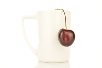 One ripe organic cherry with a white ceramic cup, close-up, isolated on white.