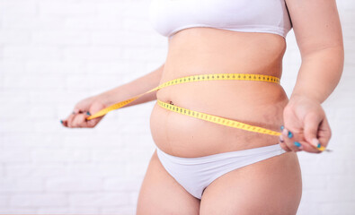 A plump woman with a tape measure tape a centimeter around her waist. Woman measures her waist fat...