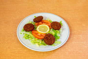 Ration of slices of falafel battered with tomato and lettuce salad served in a European Pakistani restaurant on a round plate