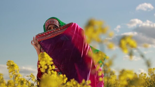 Young woman in national Afghan costume dancing in a field with yellow rapeseed flowers