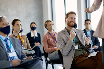 Happy businessman taking of protective face mask while talking to presenter during seminar.