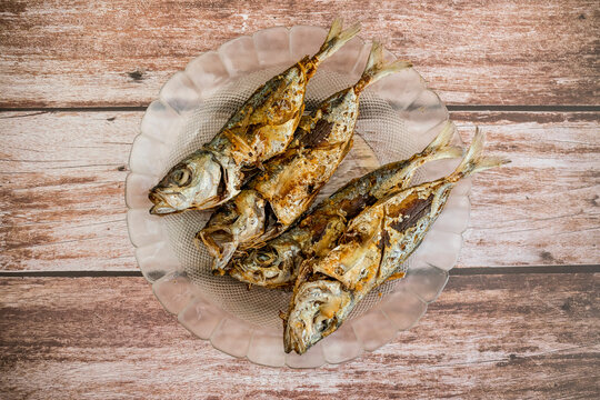 Deep fried Bigeye scad, locally known as Matang Baka. Served on a glass plate on a wood table.