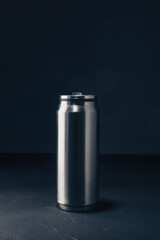 Metallic thermos bottle or thermo flask for hot or cold beverage on dark background. Eco friendly, zero waste. Vertical shot, copy space