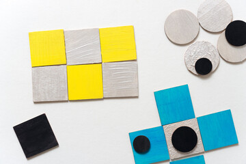 wooden shapes hand painted in yellow, pearl white, blue, and black and arranged in a loose composition on a light ground - photographed in a top-down orientation