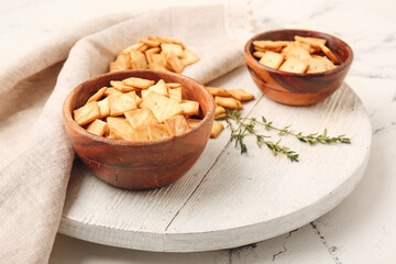 Bowls with tasty crackers on light background