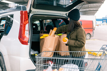 woman put bags with products in car trunk after grocery store
