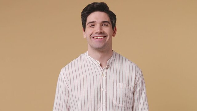 Handsome stylish brunet young man 20s years old wears white striped shirt posing look camera asides charming smile isolated on pastel beige background studio portrait People emotions lifestyle concept