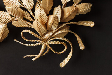 Fototapeta na wymiar The branch with leaves is made of straw. Straw wall decoration. The products are made of straw. Decoration of straw on a dark background.