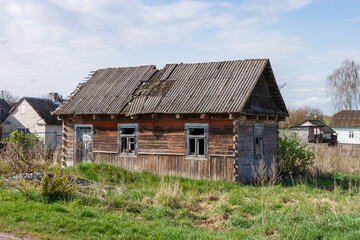 Fototapeta na wymiar Abandoned old wooden house among the trees. Rural spring landscape.