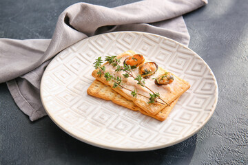Plate with tasty crackers on dark background