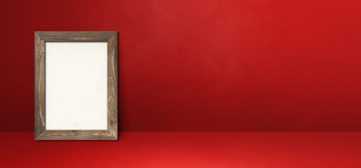 Wooden picture frame leaning on a red wall. Horizontal banner