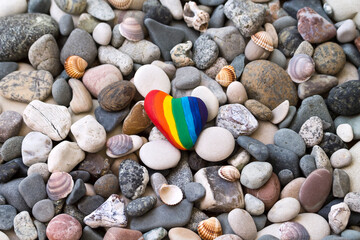 Rainbow colored heart shaped stone on the beach