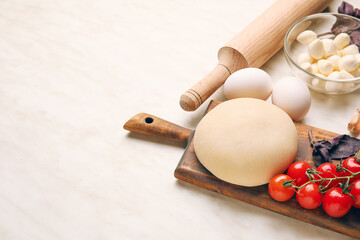 Board with dough and ingredients for preparing pizza on white background