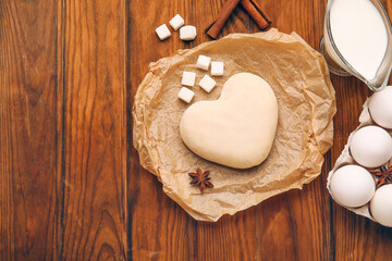 Heart shaped dough and ingredients on wooden background