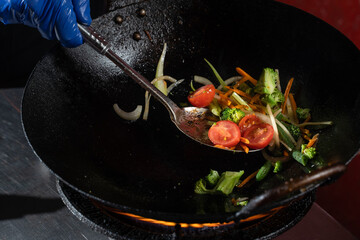 Frying vegetables in a wok pan onions, broccoli, tomatoes cherry, carrot, asparagus
