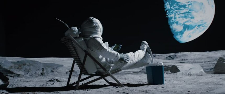 Astronaut sits in a beach chair on a Moon surface, holding phone in hands. Shot with 2x anamorphic lens