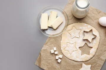 Parchment with uncooked cookies and ingredients on grey background