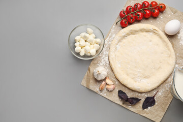 Parchment with dough and ingredients for preparing pizza on grey background