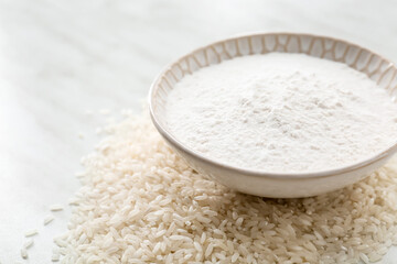 Bowl with flour and raw rice on light background