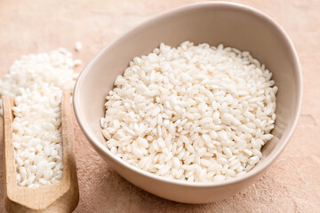 Bowl and scoop with raw rice on color background, closeup