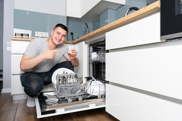 Serious young man washing dishes using dishwasher on the kitchen
