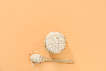 Jar and spoon with raw rice on color background