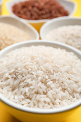 Bowls with different types of raw rice on color background, closeup