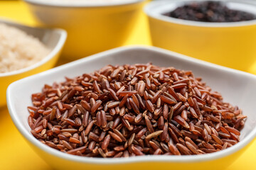 Bowls with different types of raw rice on color background, closeup