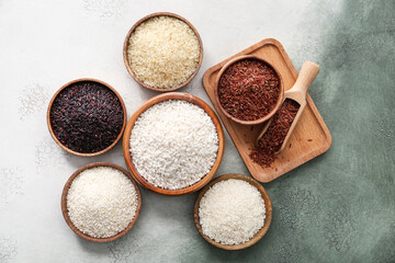 Bowls with different types of raw rice on color background