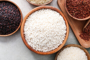Bowls with different types of raw rice on light background