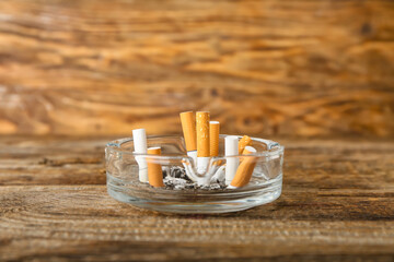 Ash tray with cigarettes on wooden background