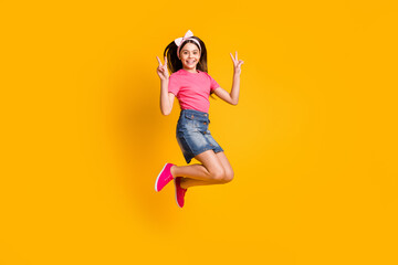 Fototapeta na wymiar Photo of funky sweet small schoolgirl dressed pink t-shirt jumping high showing two v-signs smiling isolated yellow color background