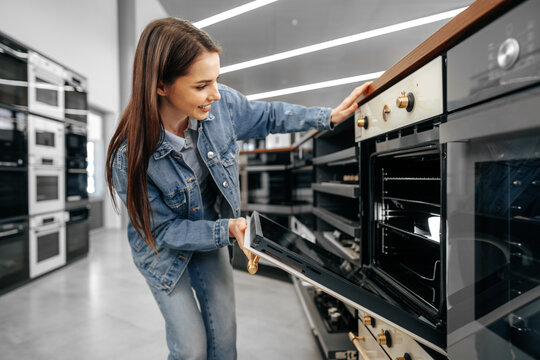 Young woman looking for new electric oven in a shopping mall