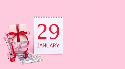 A gift box in a shopping trolley, dollars and a calendar with the date of 29 january on a pink background.