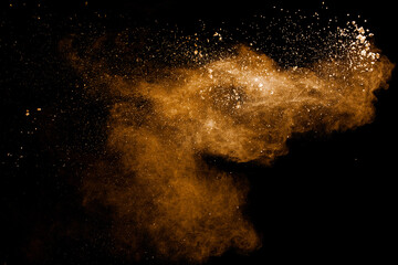 Abstract brown dust explosion on black background.Brown powder splashing.