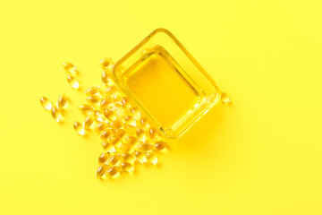 Bowl of fish oil and capsules on color background