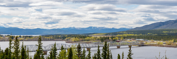 TESLIN, YUKON, CANADA Nisutlin Bay Bridge seen spanning over the river, body of water in northern Canada with mountain view in the background and large, expansive steel structure with boreal forest.