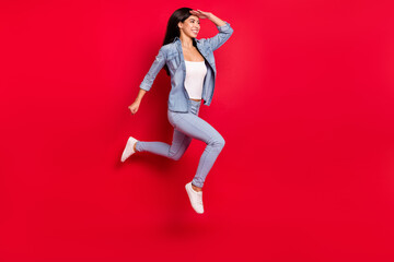Photo portrait girl in jeans outfit jumping up running fast looking far isolated on bright red color background