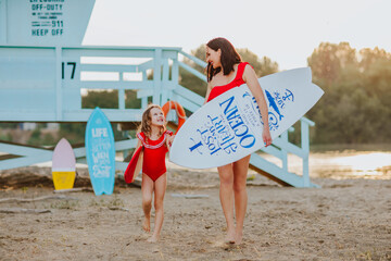 Mother and daughter holding surfboard and walking on the beach