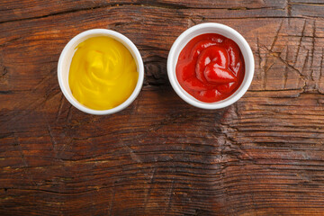 Sauce boats with cheese sauce and ketchup on a wooden table. Save a place.