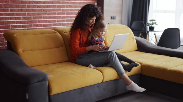 Mother and daughter sitting on the couch and typing on laptop