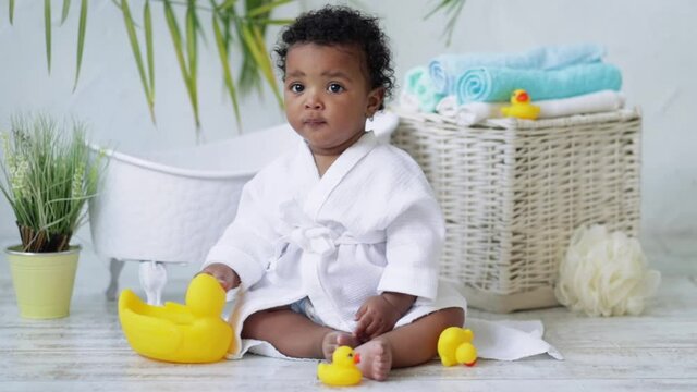 baby boy American-African plays with a rubber duck in a white coat after bathing near the bath, the concept of hygiene and child care