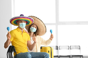 Happy couple in medical masks waiting for their flight to Mexico at the airport
