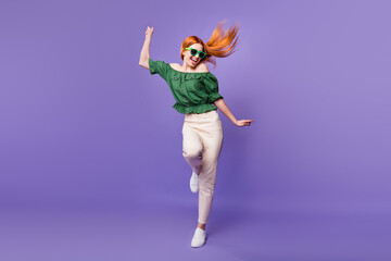 Photo of sweet funky young lady wear green blouse dark glasses smiling dancing isolated purple color background