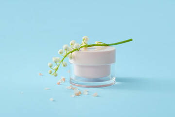 Jar of cream and lily-of-the-valley flowers on color background