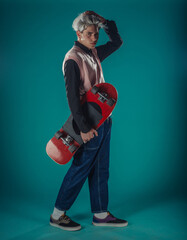 Young adult man in casual outfit wear looking at camera, holding skateboard near face and standing...
