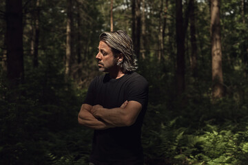 Blond man in a black t-shirt standing in the sunlight of a dense forest.