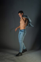 Full body portrait of sports man with denim jeans posing with bare torso in a dark studio