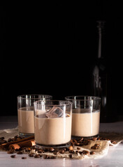 Glasses with cream liqueur and ice. Coffee beans, black bottle in the background. - obrazy, fototapety, plakaty